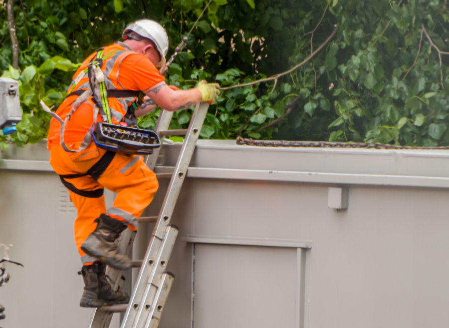 A man in a safety helmet and harness climbing a ladder.