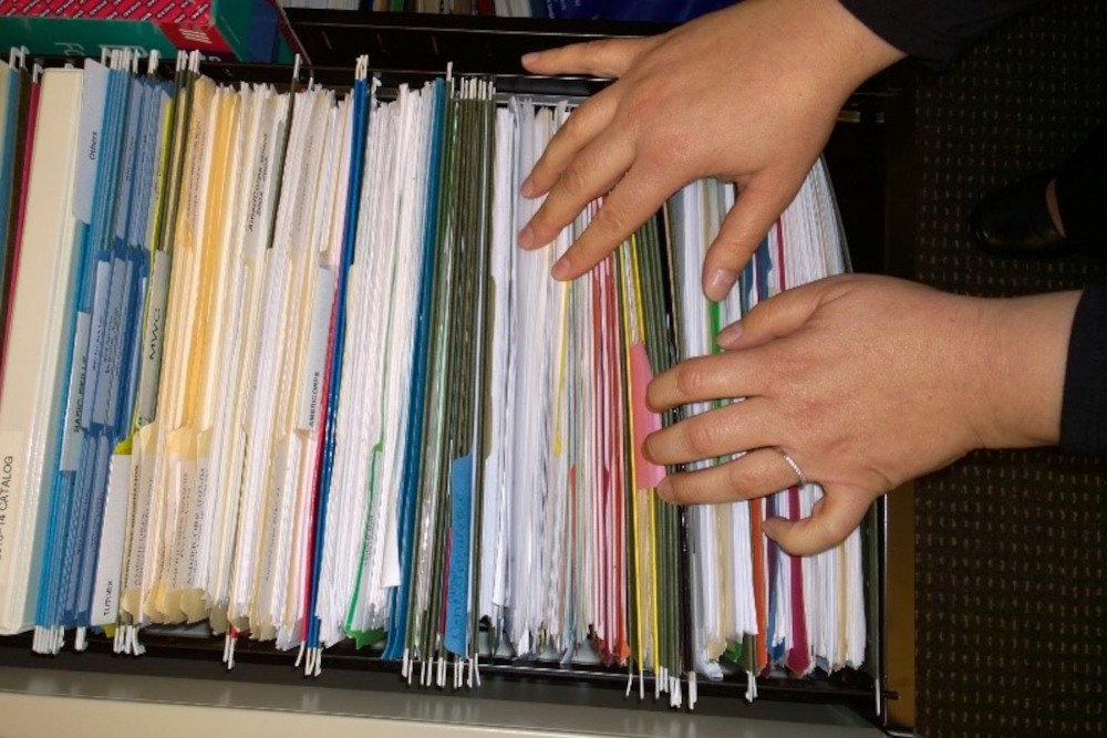 A close-up of a person looking through a full filing drawer.