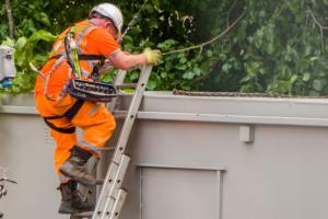 A man in a safety helmet and harness climbing a ladder.