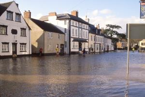 A wide street lined with a variety of buildings, all under several feet of water.